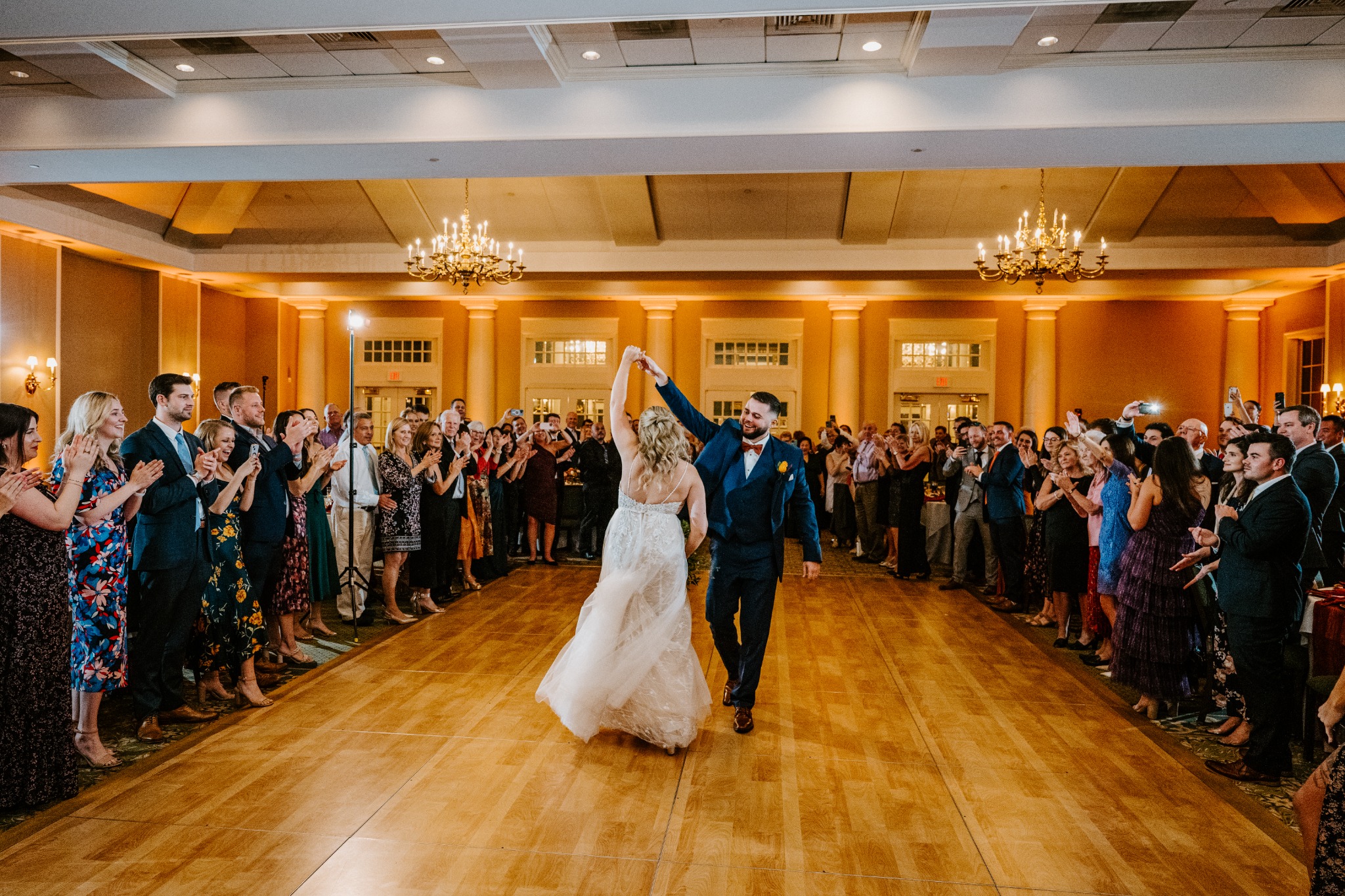 A newlywed couple dancing in a ballroom glowing with warm full-room uplighting