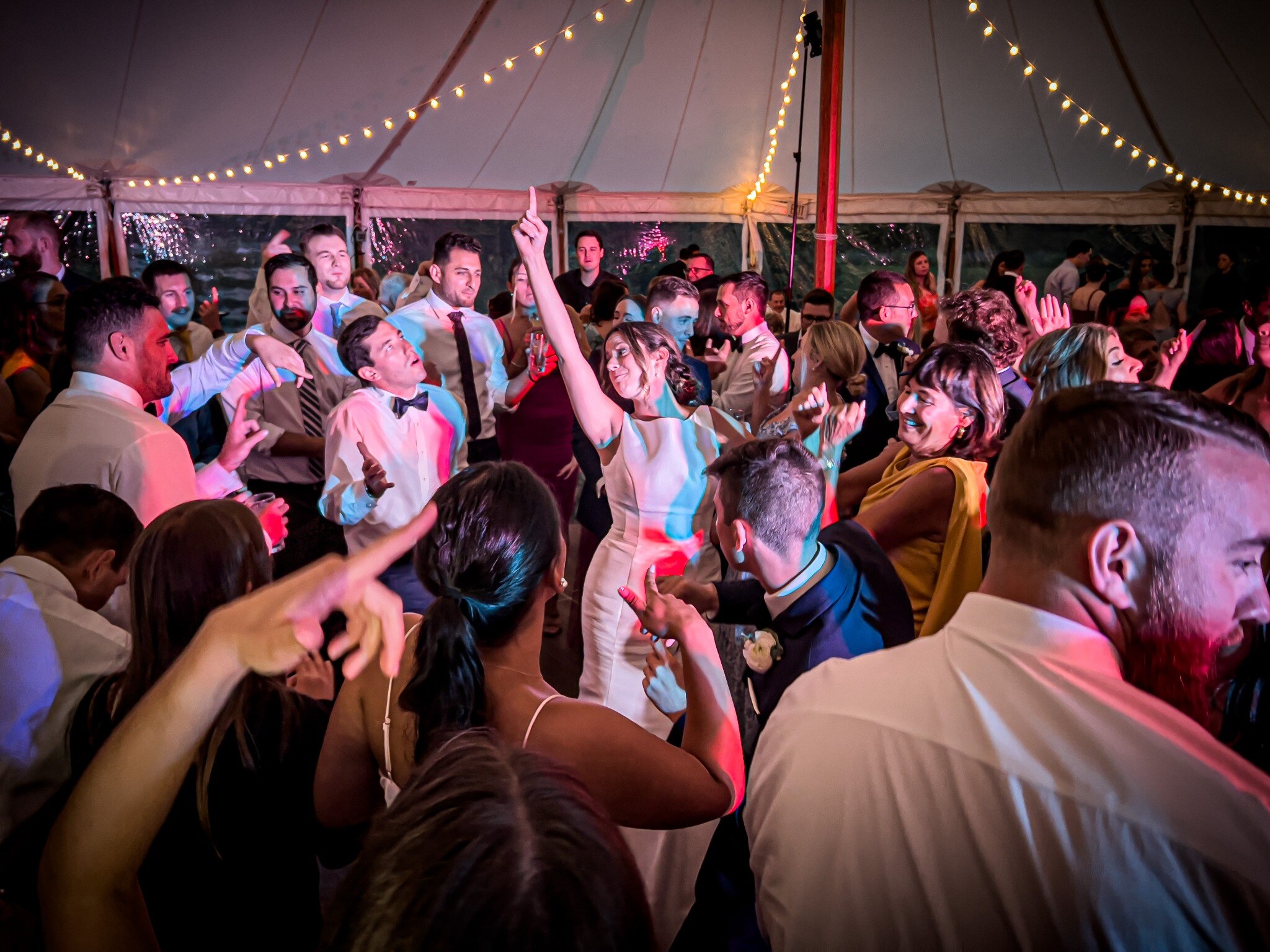 Bride celebrating in the center of a packed tented wedding dance floor