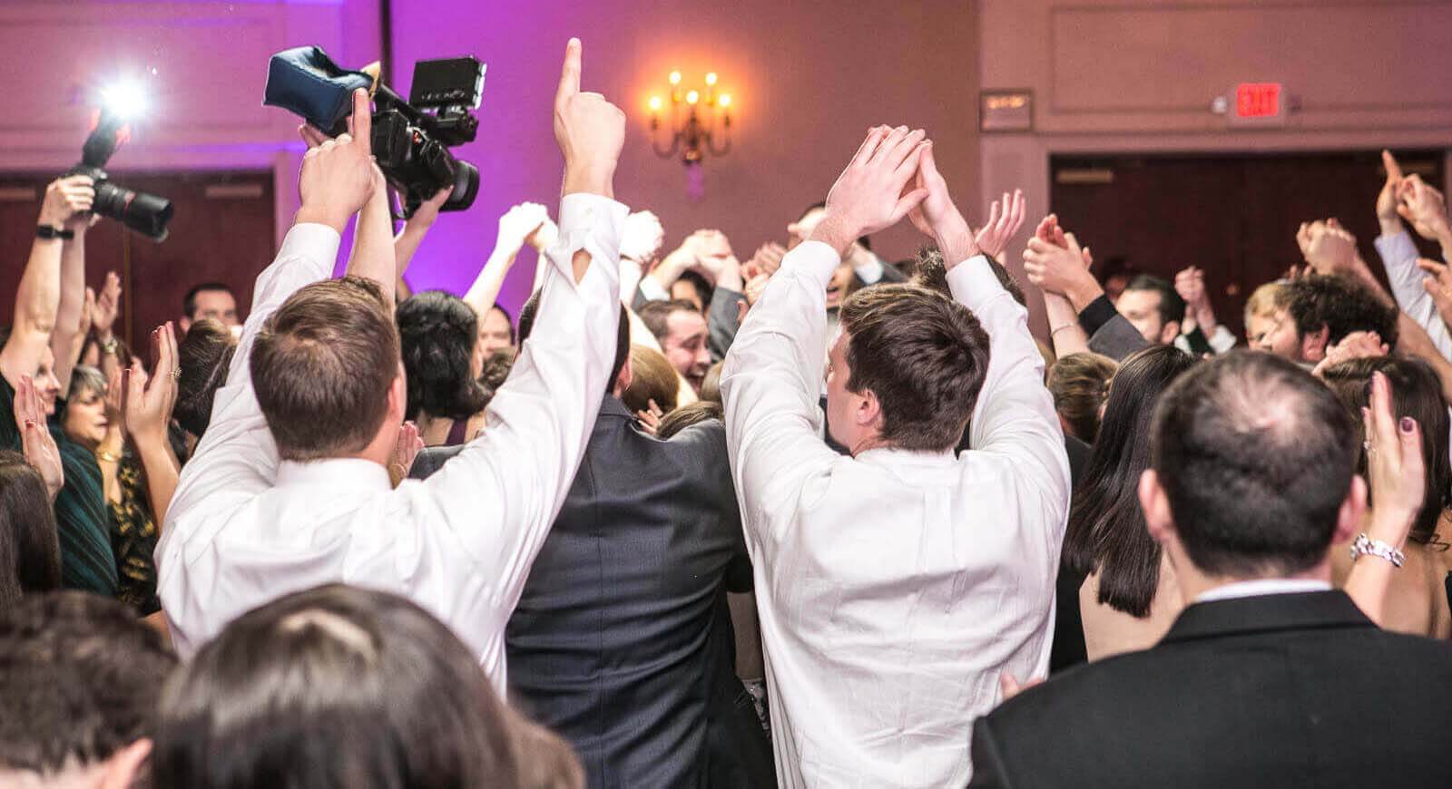 A packed wedding dance floor being filmed by a videographer